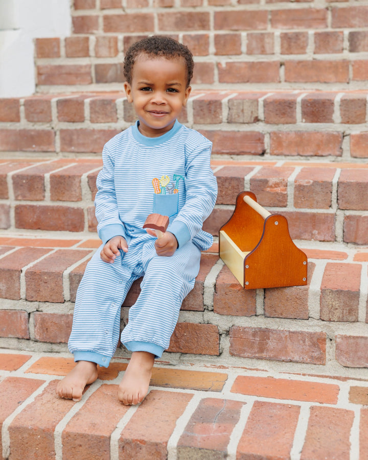 Child in blue pajamas sitting on brick steps with a wooden toy.