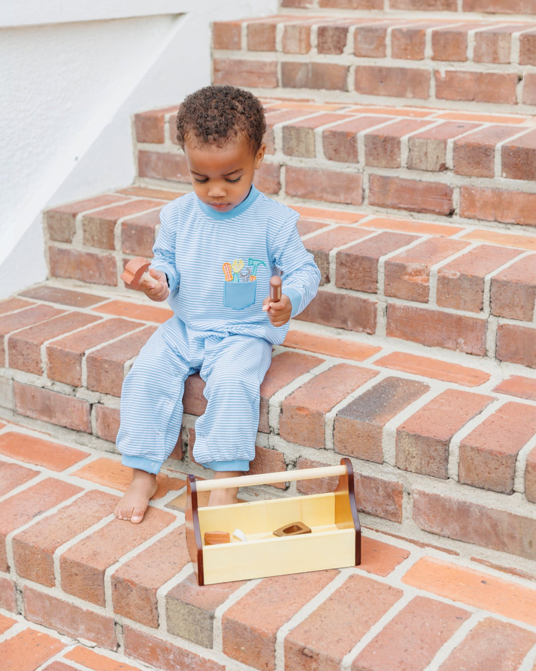 Child sitting on a set of brick steps with a wooden toy box in front