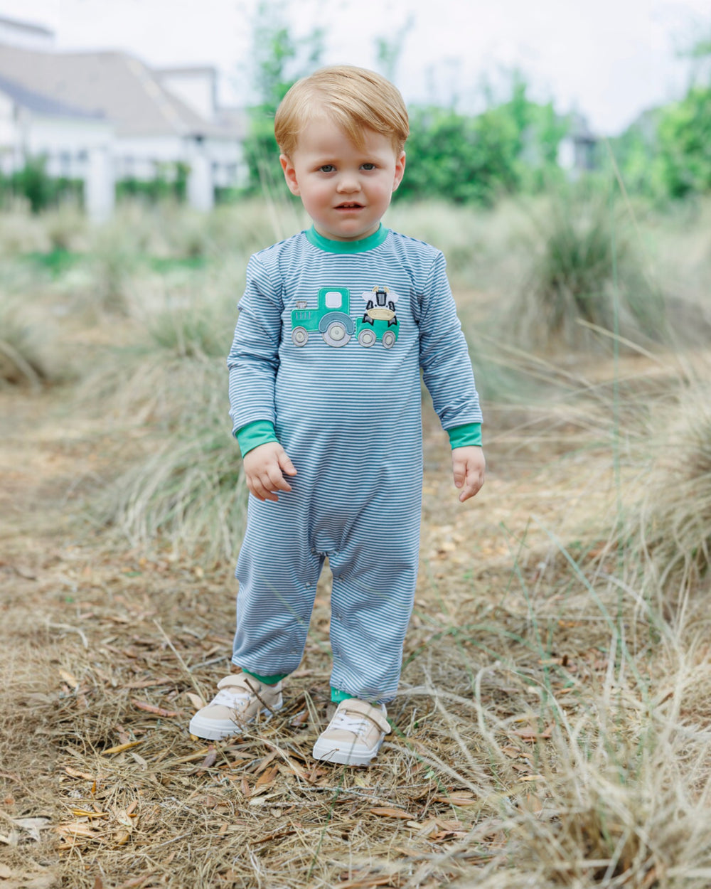 Child wearing a blue striped onesie with a truck design outdoors