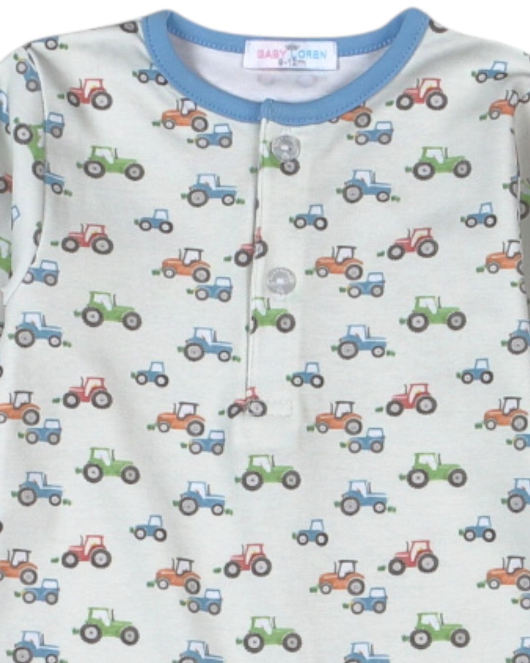 A close-up of a baby long-sleeve top featuring an all-over tractor print on a light cream background, with a contrasting light blue ribbed crew neck and a three-button henley front, that store