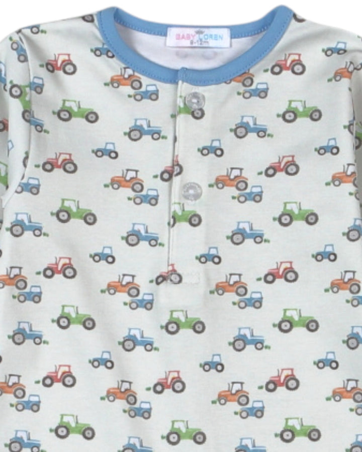 A close-up of a baby long-sleeve top featuring an all-over tractor print on a light cream background, with a contrasting light blue ribbed crew neck and a three-button henley front, that store
