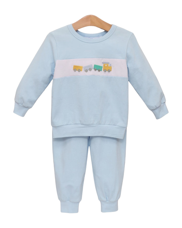 A two-piece baby loungewear set in light blue, featuring a long-sleeve sweatshirt with a horizontal white stripe across the chest containing small colorful train illustrations, and matching jogger pants, displayed on a wooden hanger against a white background, that store