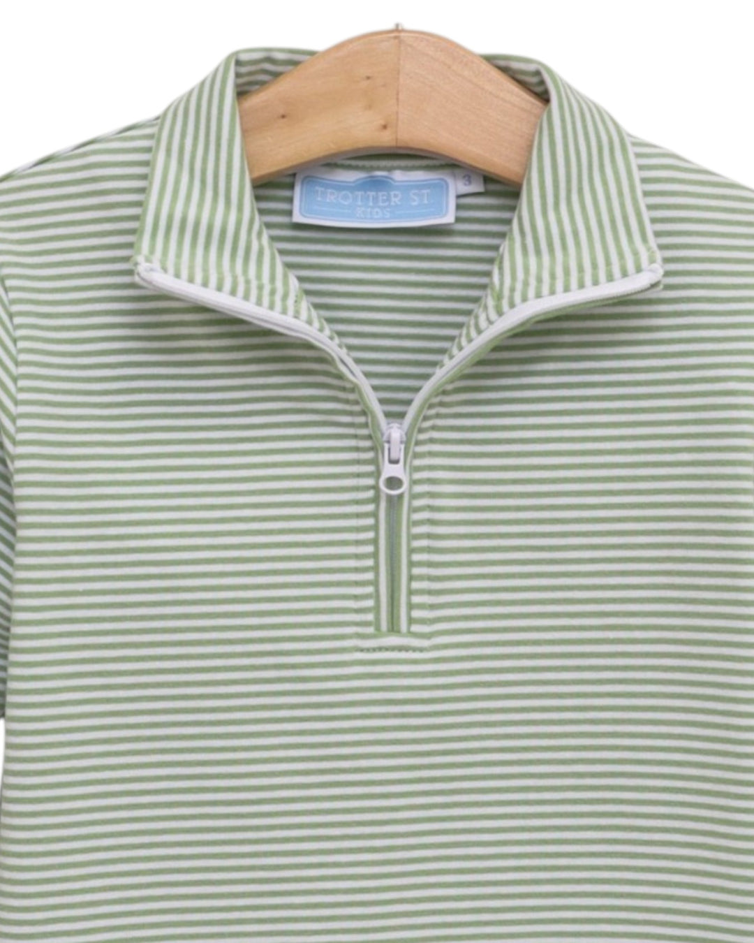 A close-up of a green and white striped quarter-zip polo shirt hanging on a wooden hanger. The shirt features a stand-up collar with white piping and a silver zipper, that store