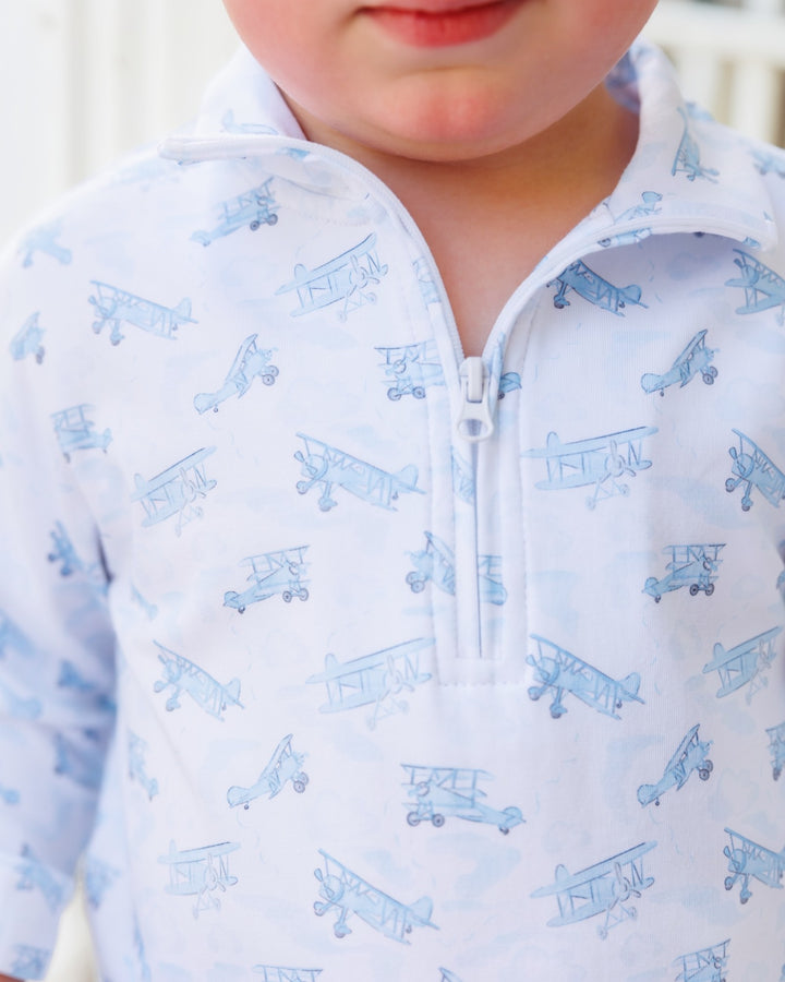 Close-up of a child wearing a white long-sleeve quarter-zip pullover with a light blue repeating biplane print.