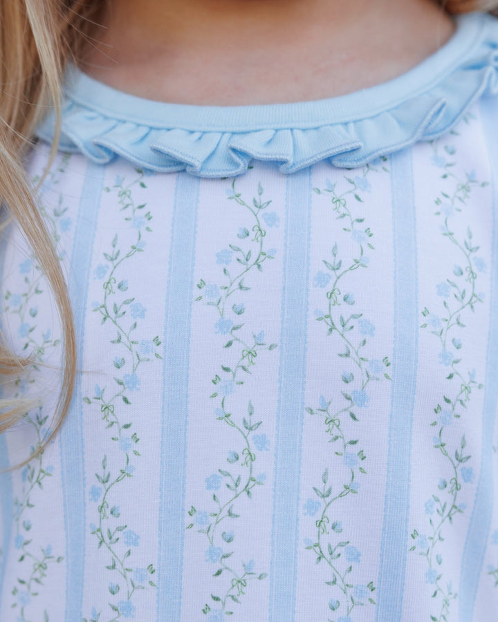 Close-up of a child wearing a light blue ruffled collar top with vertical light blue stripes and a delicate green and blue floral print, that store