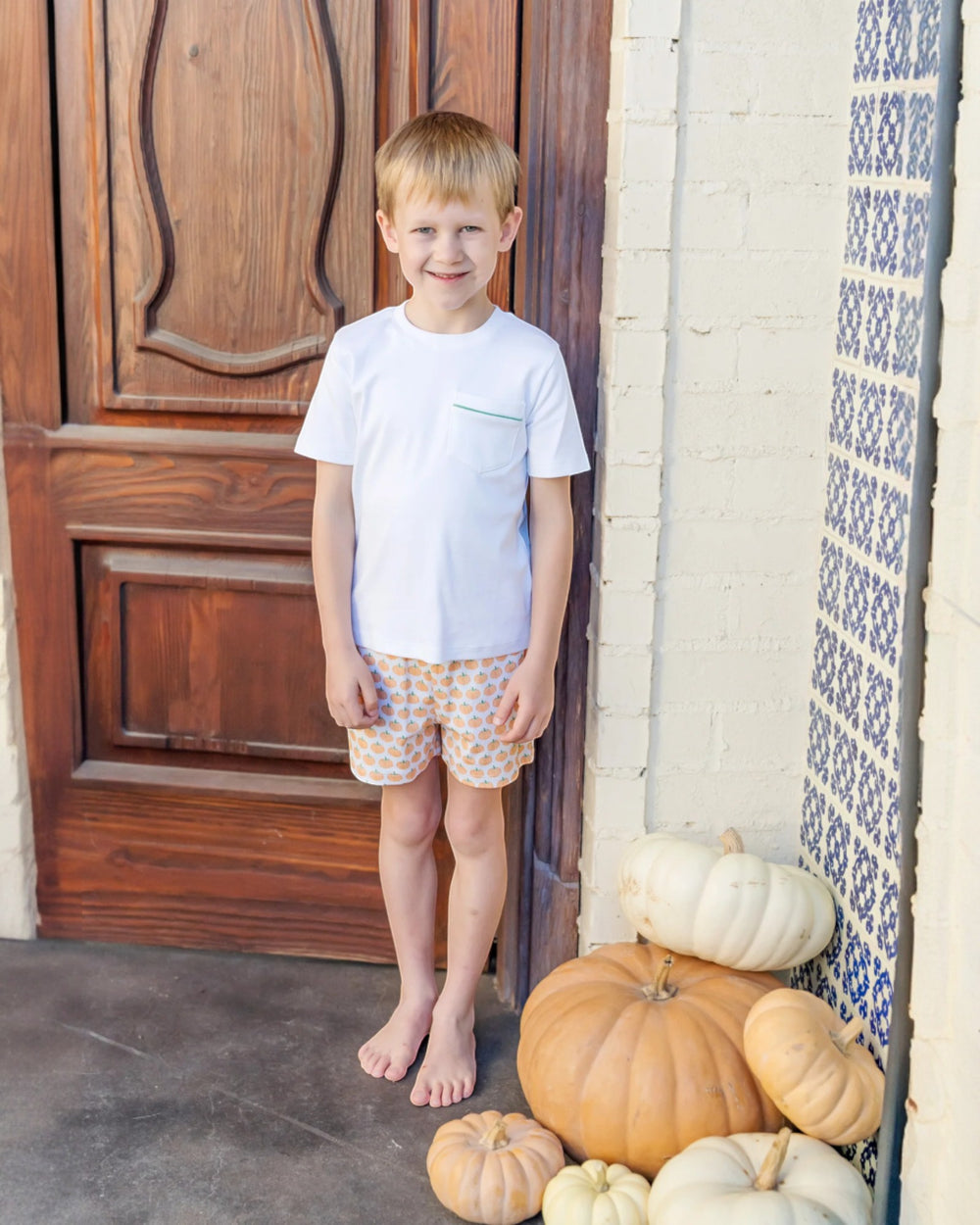 Young boy standing next to pumpkins on a porch