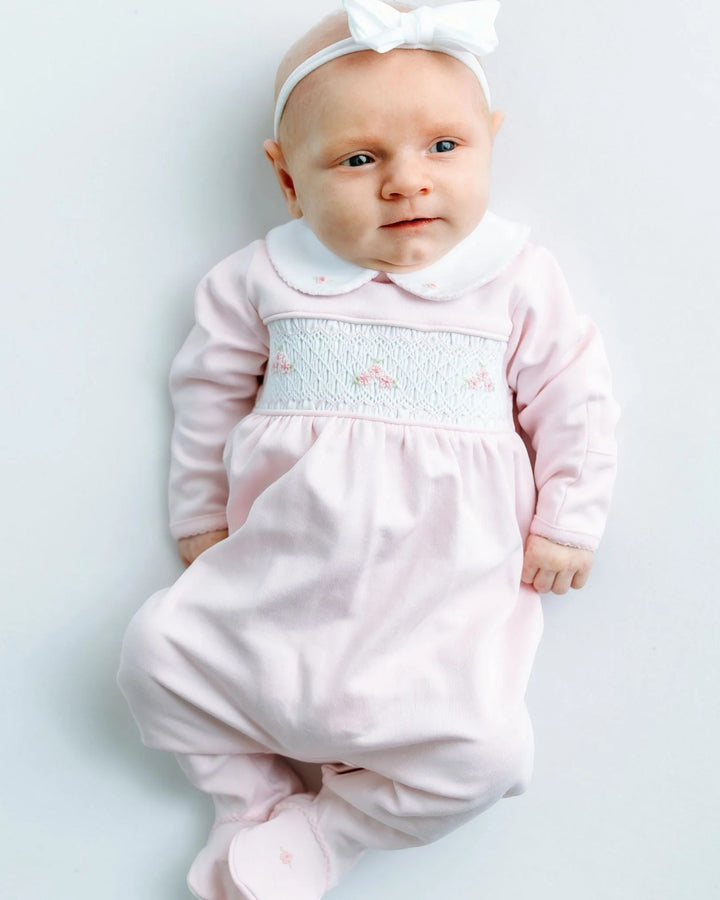 Baby in a pink outfit with smocking on a light gray background