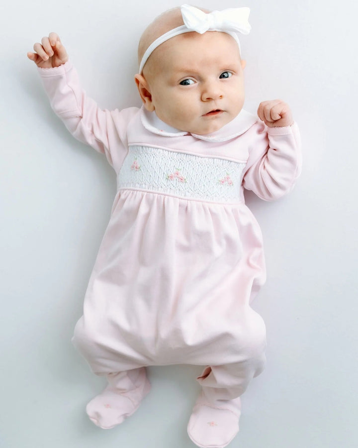 Baby in a pink outfit with a white bow on a light gray background