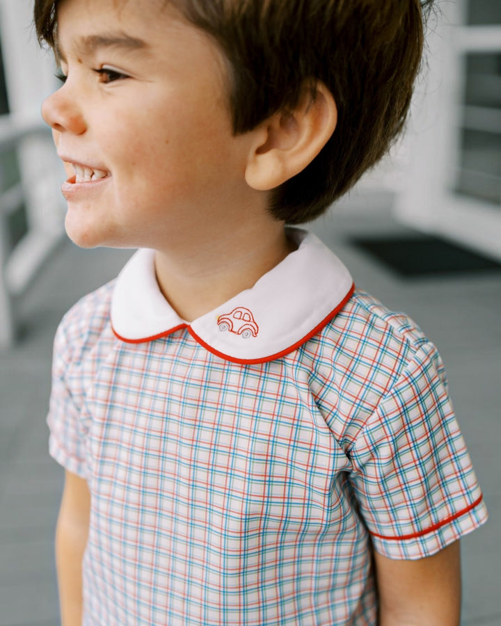 Child wearing a checkered shirt with a white collar featuring a red border and embroidered design.