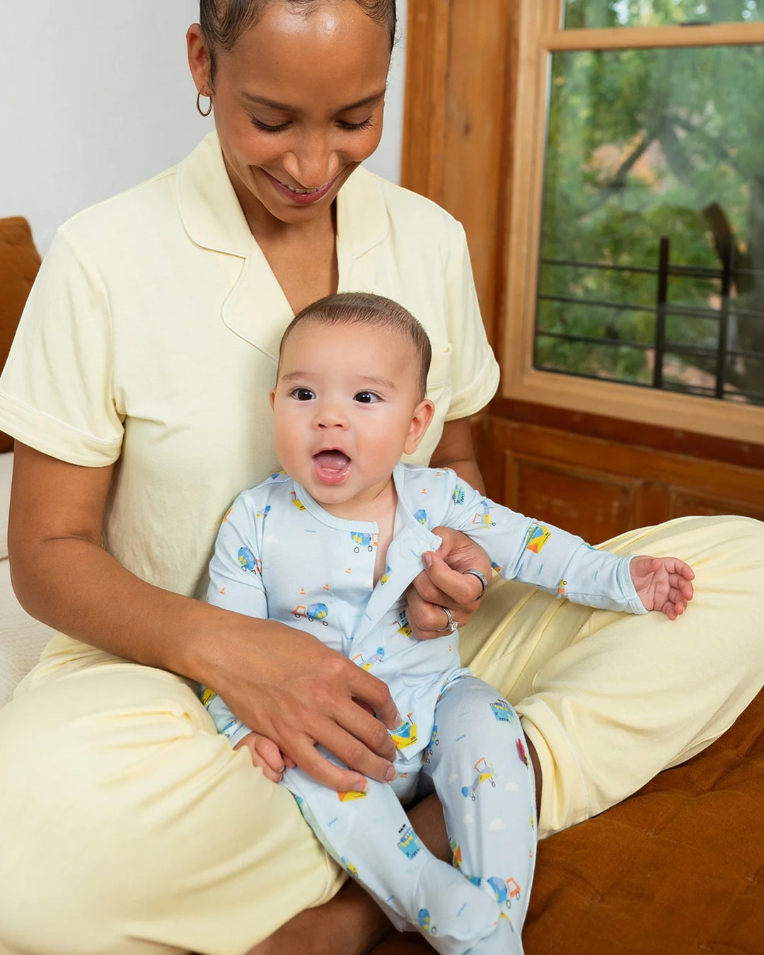 Woman holding a baby in a room with a window and furniture.