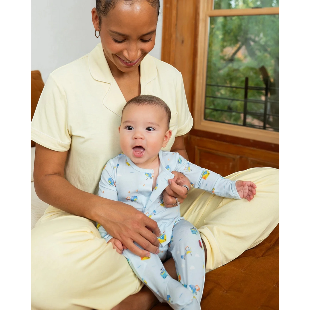 Woman holding a baby in a room with a window and furniture.