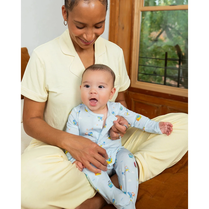Woman holding a baby in a room with a window and furniture.