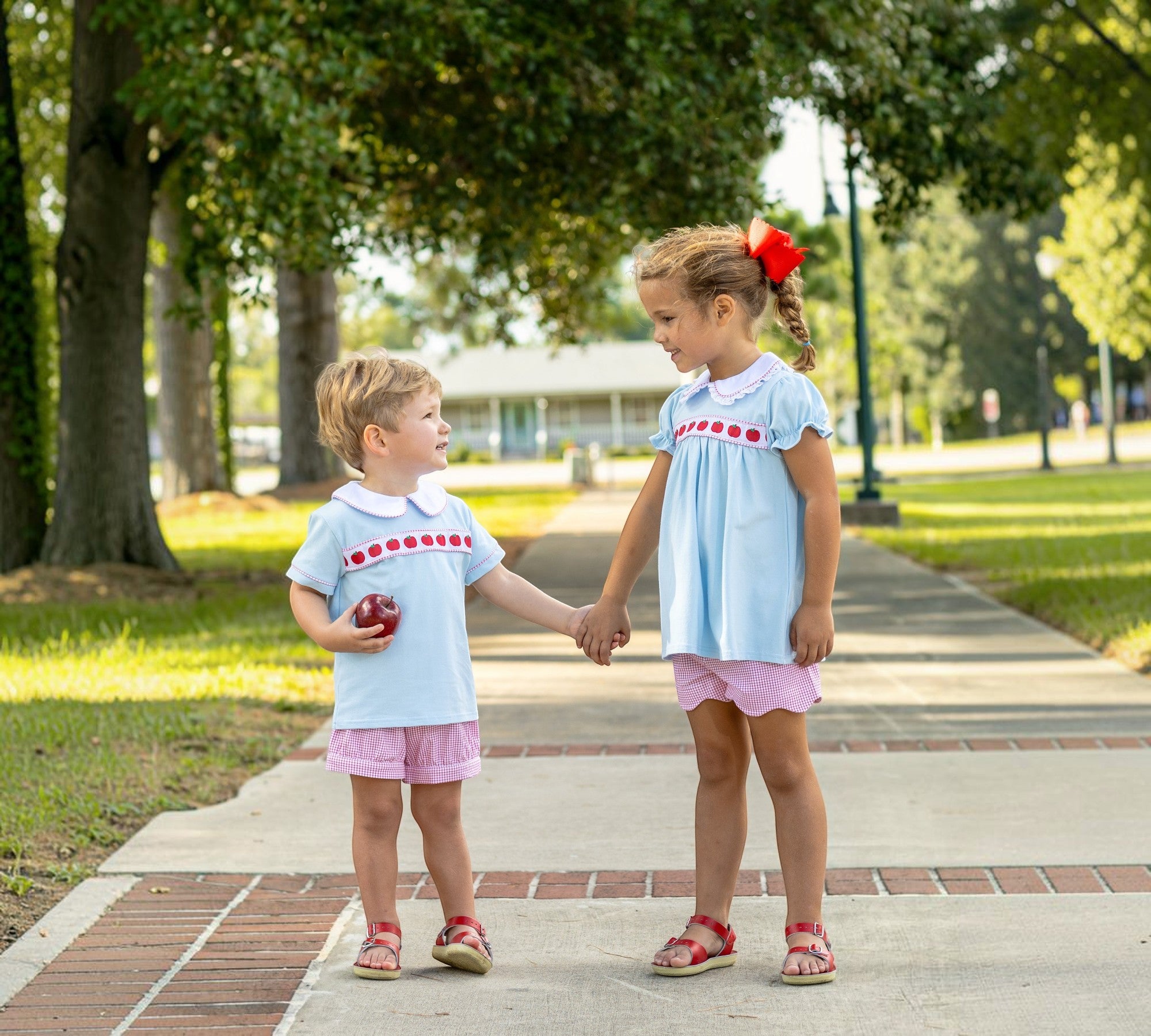 Two children holding hands on a sidewalk in a park.