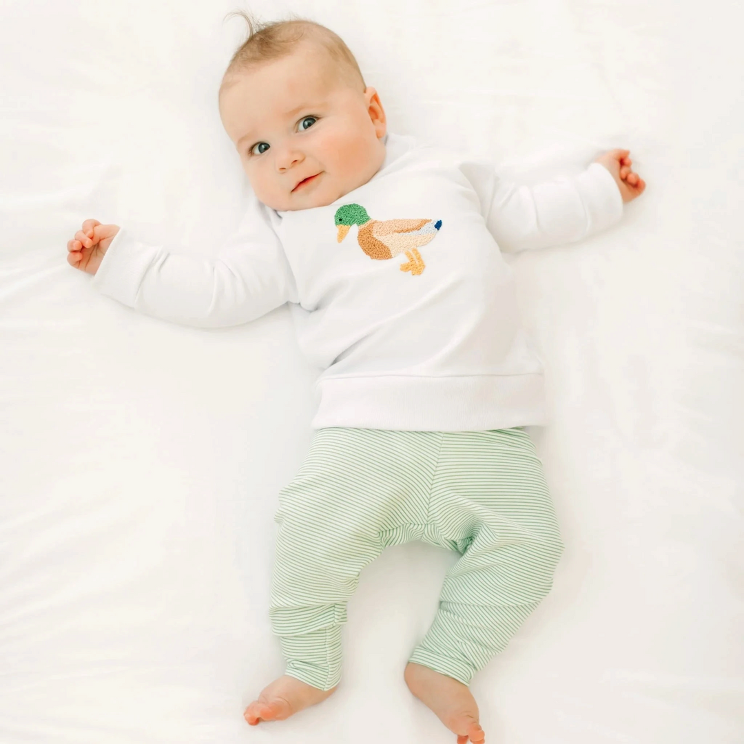 Baby wearing a white That Store Pima cotton sweatshirt with a detailed mallard duck embroidery and green striped pants.