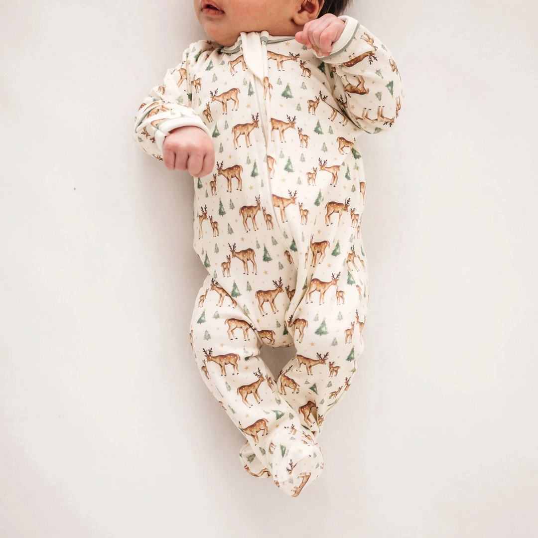 That Store baby footie in ivory Pima cotton with a woodland deer, fawn, and evergreen tree print and moss green trim.