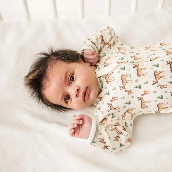 That Store baby footie in ivory Pima cotton with a woodland deer, fawn, and evergreen tree print.