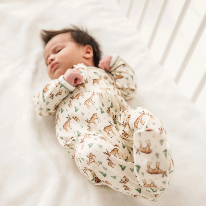 Baby sleeping in a That Store ivory Pima cotton footie with a woodland deer and evergreen tree print.