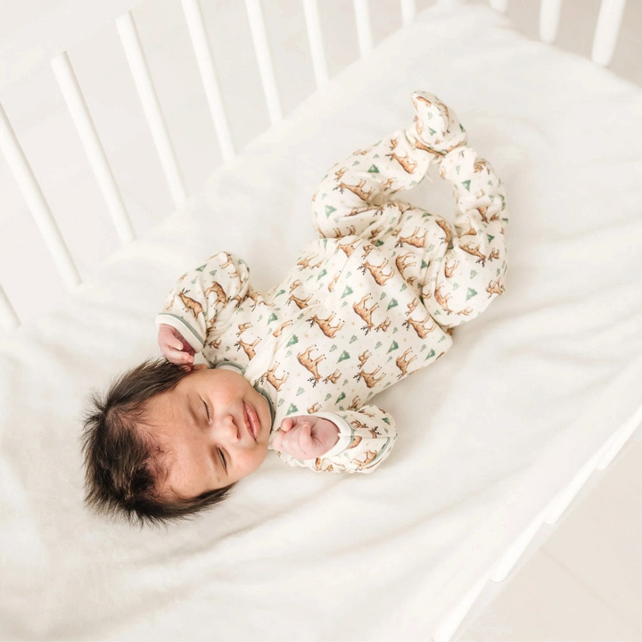 That Store ivory Pima cotton baby footie with woodland deer print and moss green trim, worn by a sleeping newborn.