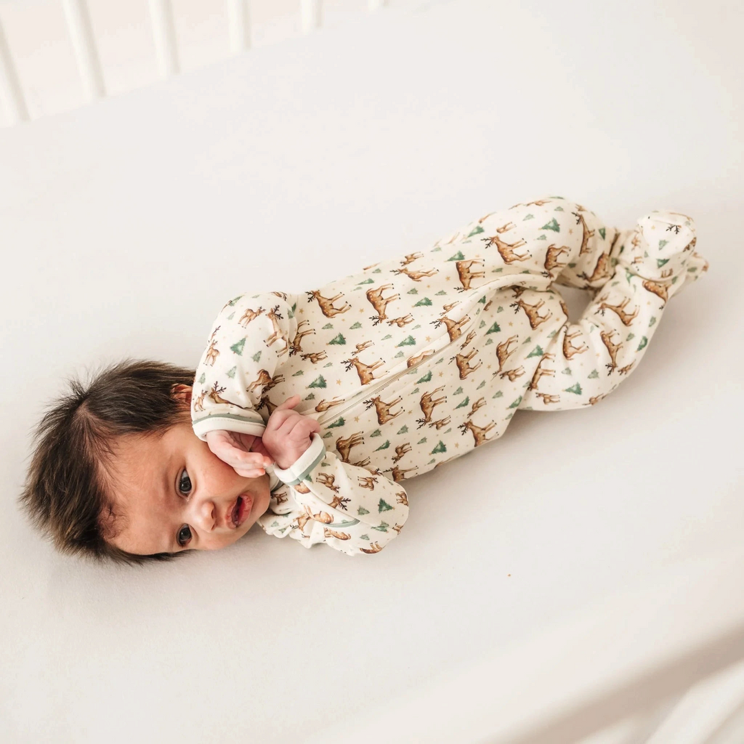 Baby wearing a That Store ivory Pima cotton footie with a woodland deer, tree, and star print and moss green trim.
