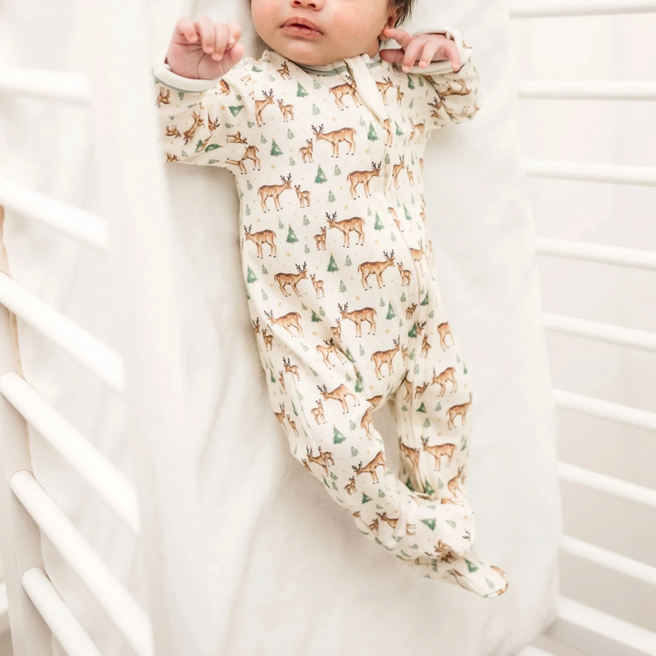 That Store baby footie in ivory Pima cotton with a woodland deer, fawn, and evergreen tree print and moss green trim.