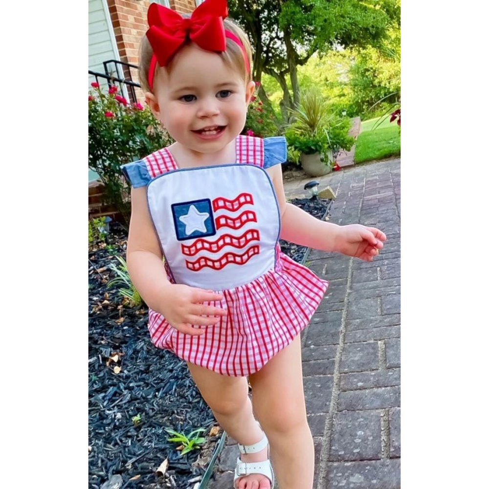 Toddler girl wearing a That Store American flag bubble with red windowpane gingham, chambray ruffles, and a red bow.
