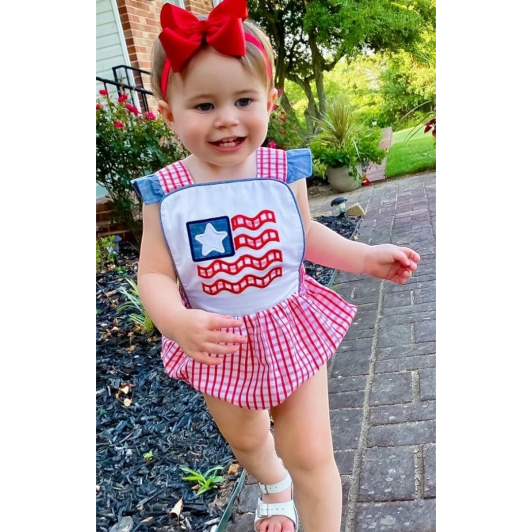 Toddler girl wearing a That Store American flag bubble with red windowpane gingham, chambray ruffles, and a red bow.