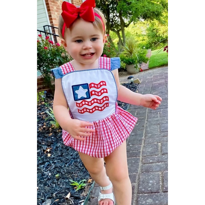 Toddler girl wearing a That Store American flag bubble with red windowpane gingham, chambray ruffles, and a red bow.