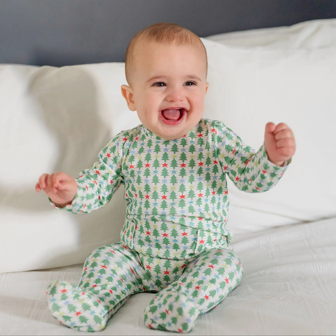 A happy baby wearing a That Store long-sleeve footed romper with a festive green Christmas tree and star print.