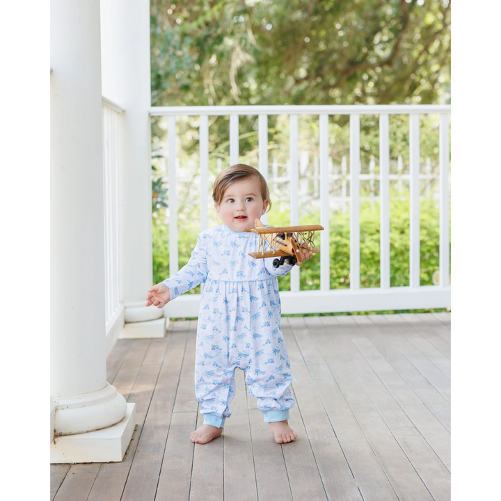 That Store baby boy wearing a blue airplane print cotton romper while holding a wooden toy plane on a porch