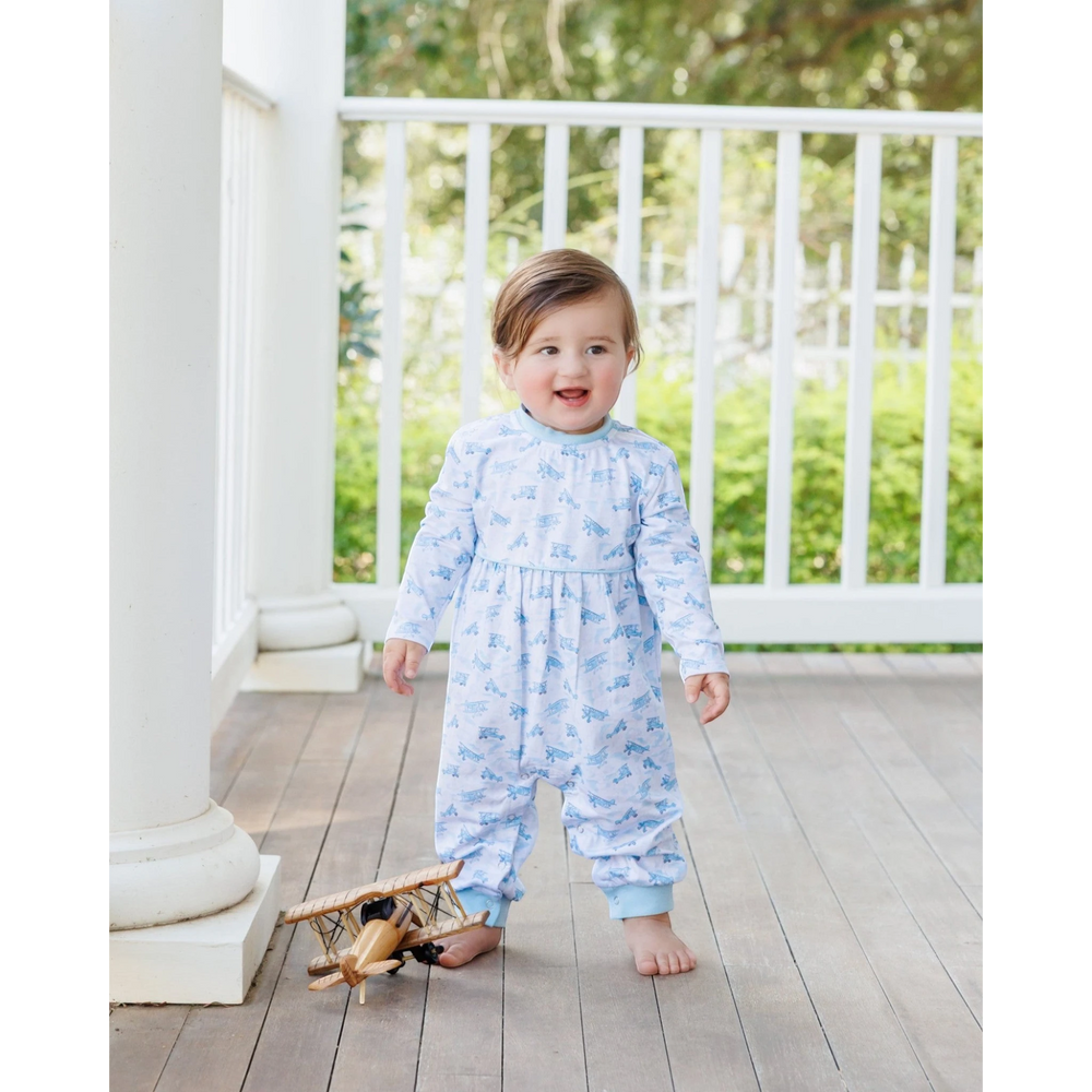 That Store blue airplane print cotton romper worn by a toddler standing on a porch with a toy wooden airplane