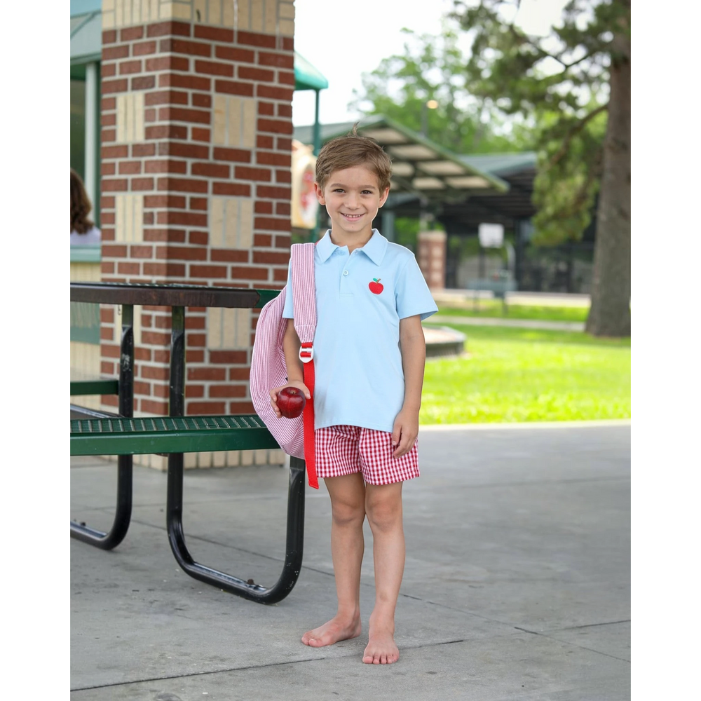 That Store light blue polo shirt with apple embroidery worn by a young boy with a red striped backpack