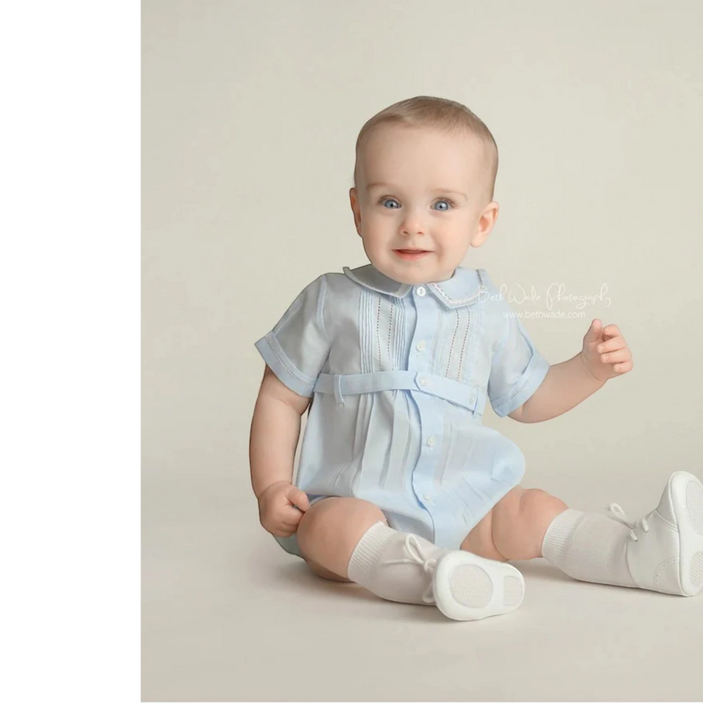 That Store baby boy blue creeper with ric-rac trim, pintucks, and button-down front, worn by a seated baby.