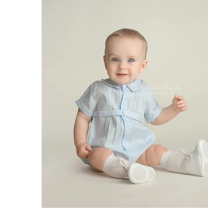 That Store baby boy blue creeper with ric-rac trim, pintucks, and button-down front, worn by a seated baby.
