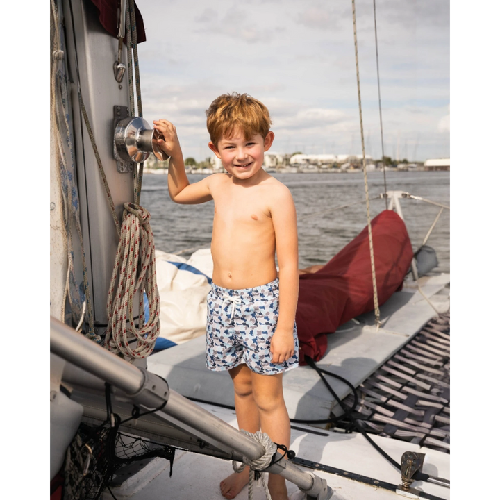 Young boy wearing That Store blue camo Saint Simons swim trunks while standing on a sailboat deck.