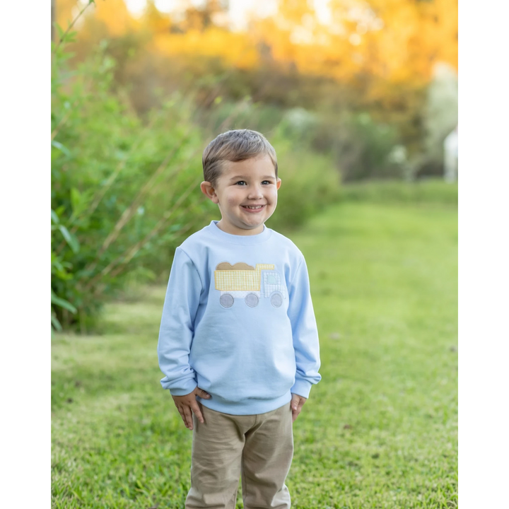 That Store blue French terry pullover for boys featuring a yellow dump truck graphic, worn in a grassy outdoor park.