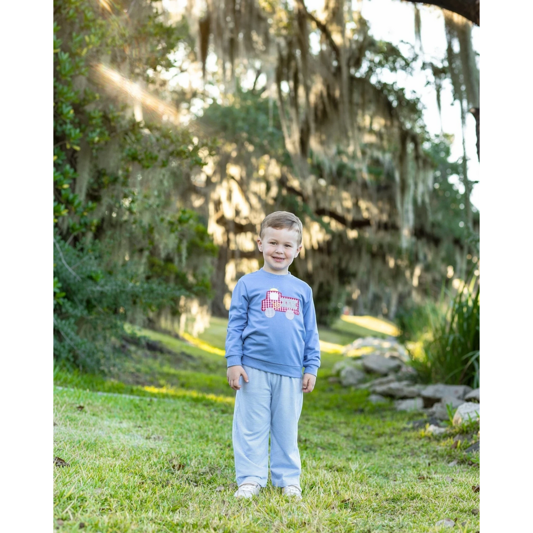 A young boy wearing a That Store blue French terry pullover with a red fire truck design and striped pants outdoors.