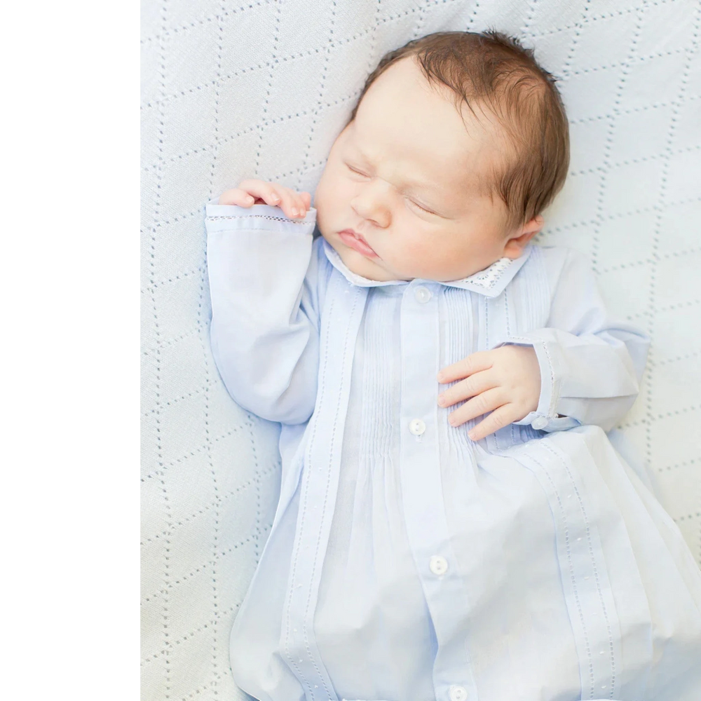 Newborn baby boy sleeping in a That Store blue take me home gown with pintuck details and a pointed collar.