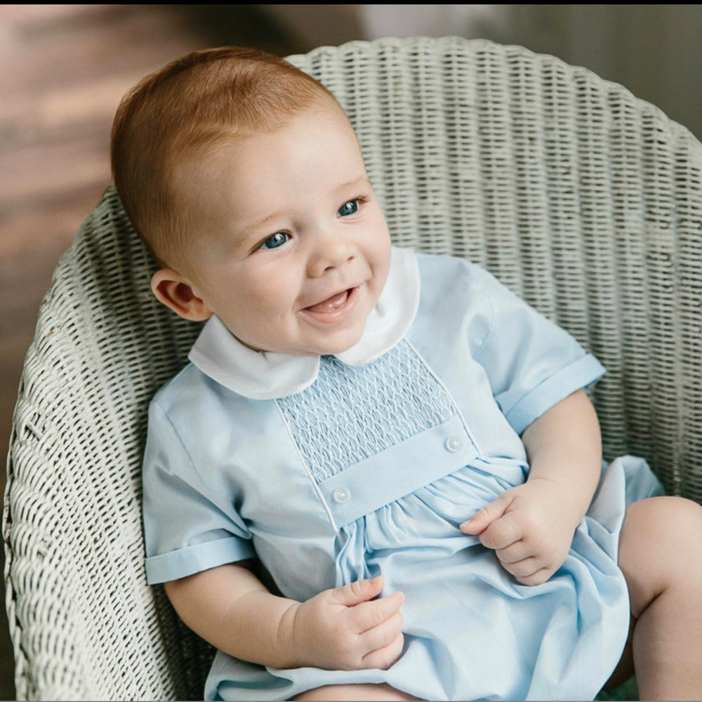 That Store baby boy wearing a light blue creeper with chevron smocking, white pique collar, and tuxedo-style buttons.