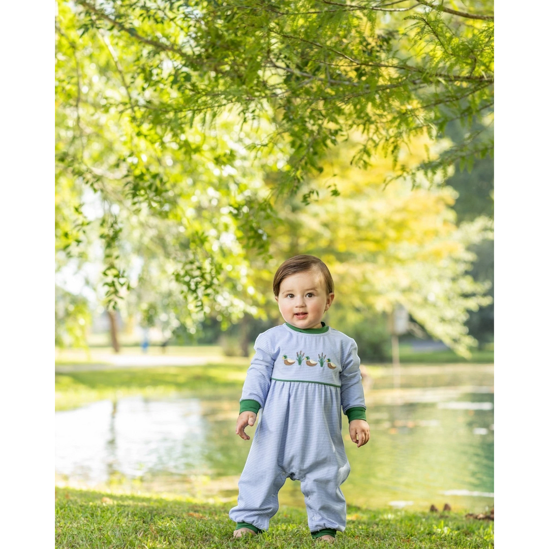 That Store blue striped cotton romper with mallard duck embroidery worn by a toddler standing in a park.