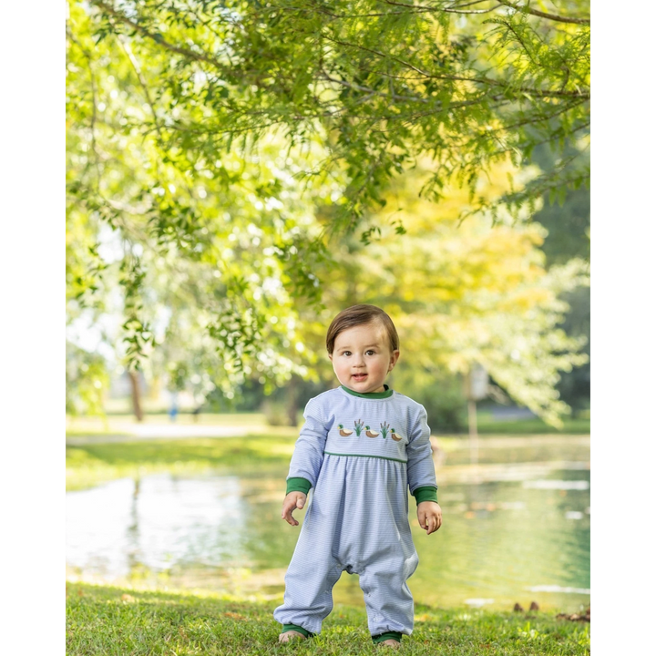 That Store blue striped cotton romper with mallard duck embroidery worn by a toddler standing in a park.