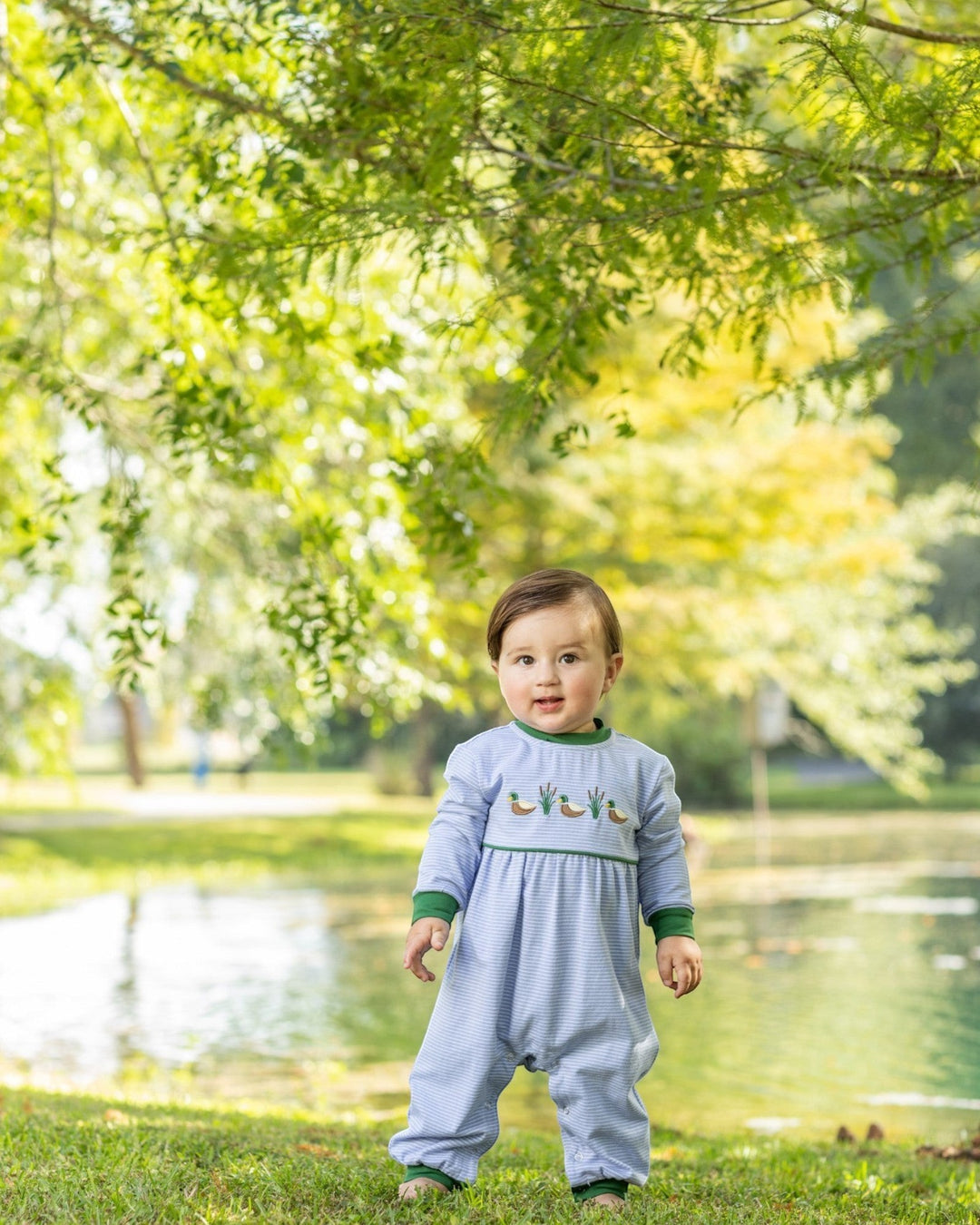 That Store blue striped cotton romper with mallard duck embroidery worn by a toddler in a park setting.