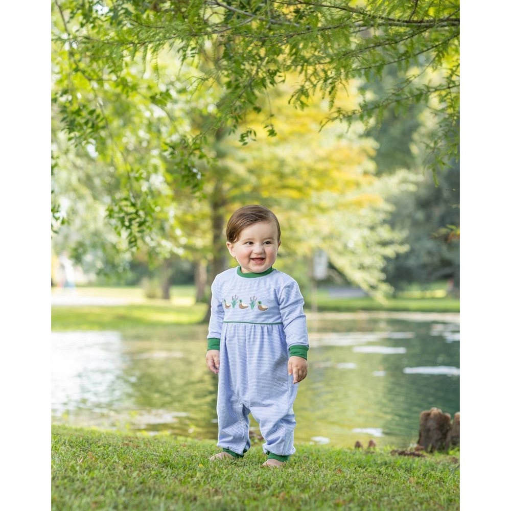 A smiling baby wearing a That Store blue striped cotton romper with embroidered mallard ducks in a park setting.