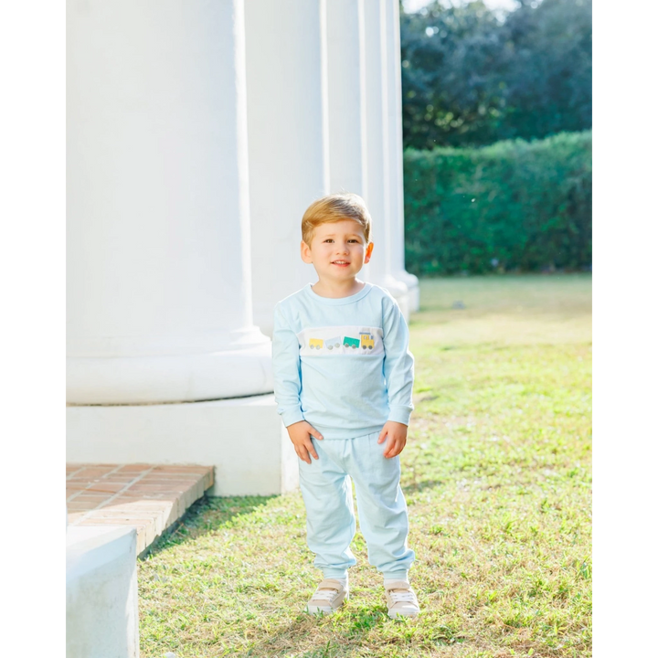 A young boy wearing a That Store light blue jogger set with a whimsical embroidered train design on the chest.