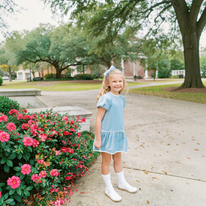 Young girl wearing a That Store Beaufort blue velvet dress with white trim and a matching bow in an outdoor park