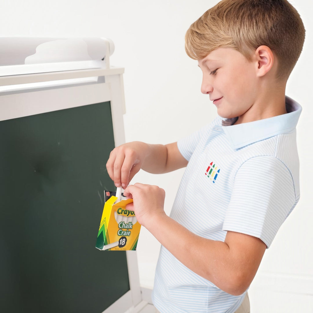 That Store boys blue striped polo shirt with crayon embroidery worn by a boy holding a box of chalk by a chalkboard