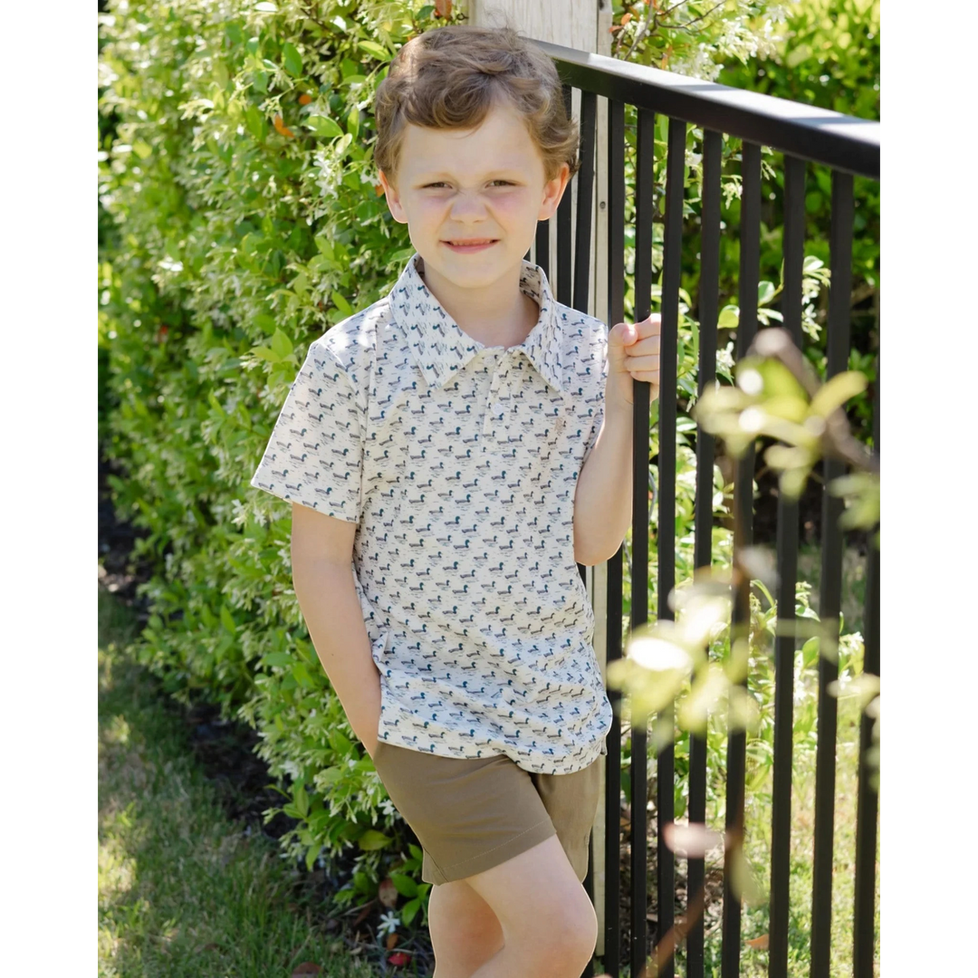 Boy wearing That Store Performance Henry polo with mallard duck print on cream fabric, paired with brown shorts