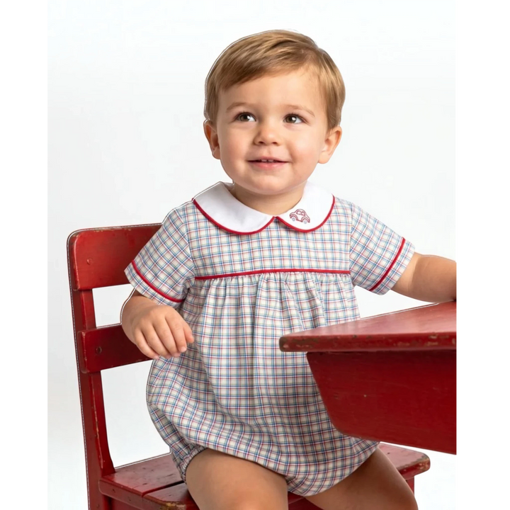 That Store boys bubble in primary plaid with red trim and car embroidery, worn by a toddler sitting at a red desk.