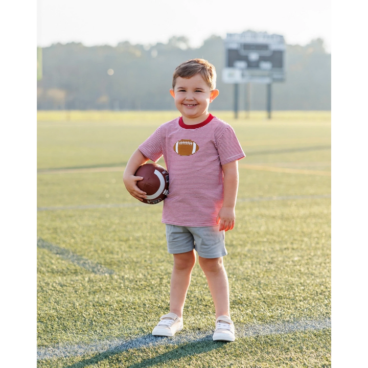 That Store boys red striped football applique t-shirt worn by a smiling child holding a football on a sports field.