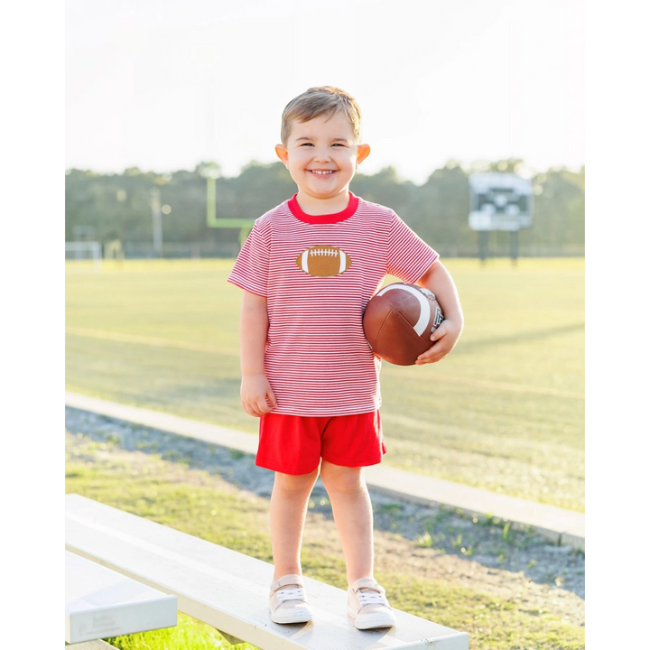 That Store boys red and white striped cotton football applique t-shirt worn by a smiling boy on a sports field.