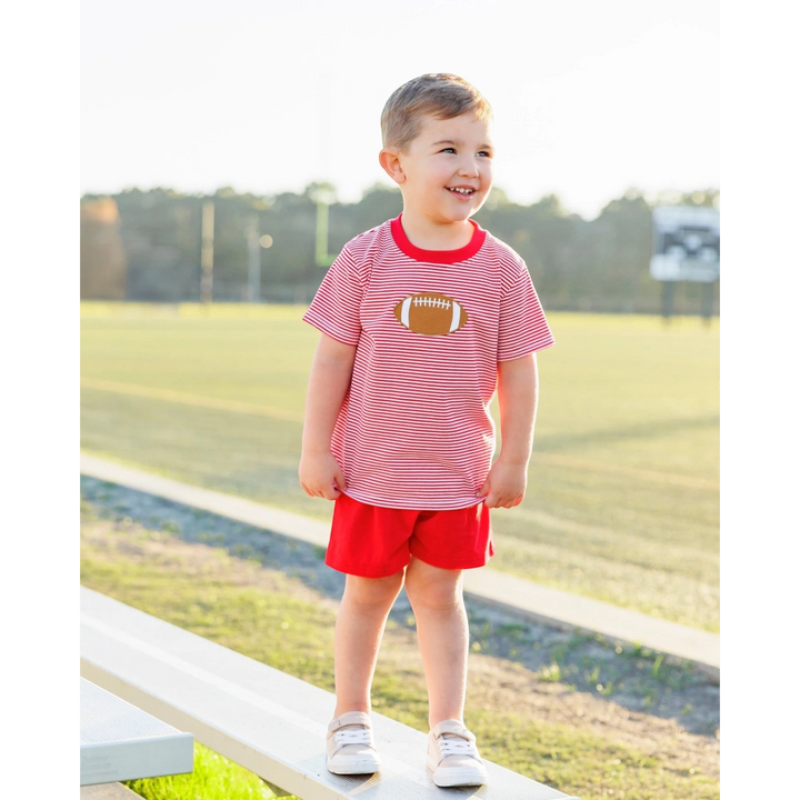 That Store boys red striped football applique t-shirt worn by a smiling toddler on a sunny sports field